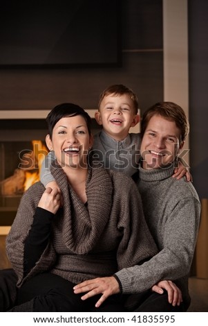 Happy family sitting on couch at home in a cold winter day, looking at camera, laughing.