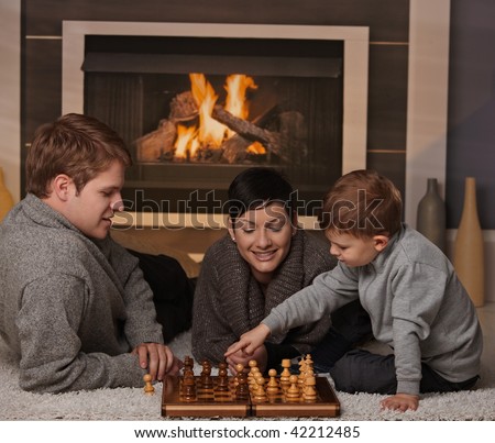 Young family with 4 years old kid playing chess at home in a cold winter day.