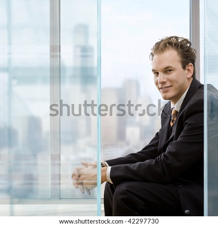 Profile portrait of businessman talking sitting in modrn office in front of windows, smiling.