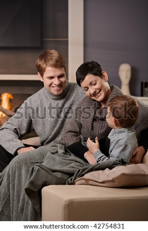 Happy family sitting on sofa at home in front of fireplace, smiling.