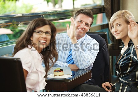 Young businessman and businesswomen having a meeting in cafe, smiling and waving to somebody.