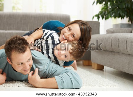 Happy family playing at home, lying heaped on floor in living room.