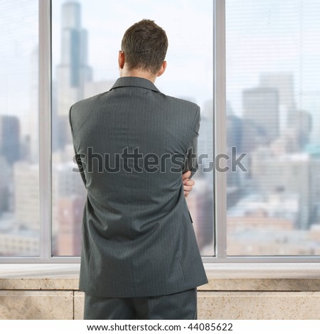 Businessman thinking in office, looking out of windows to downtown vista.