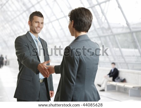 Smiling businessman and businesswoman shaking hands in hallway.