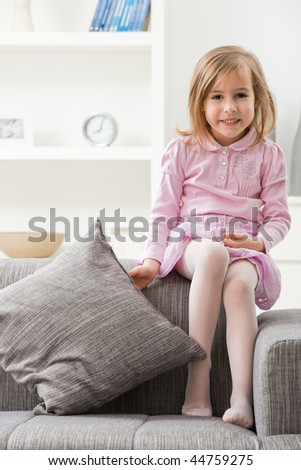Portrait of happy little girl in pink dress, sitting on couch, smiling.