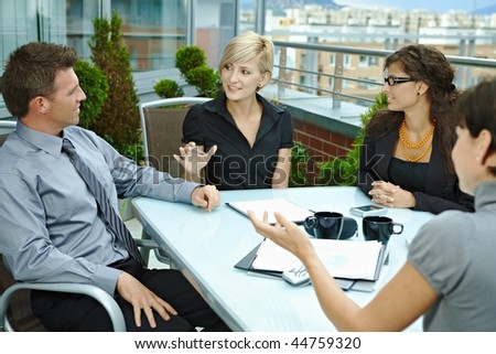 Group of young business people sitting around table on office terrace outdoor, talking and working together.