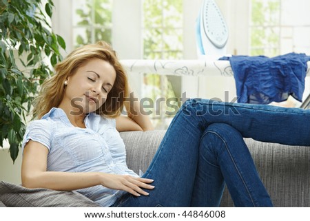 Tired young woman resting on couch, having a break during housework.