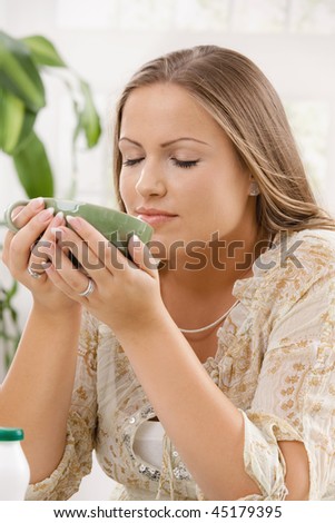 Beautiful young woman drinking tea, holding the cup with both hands.