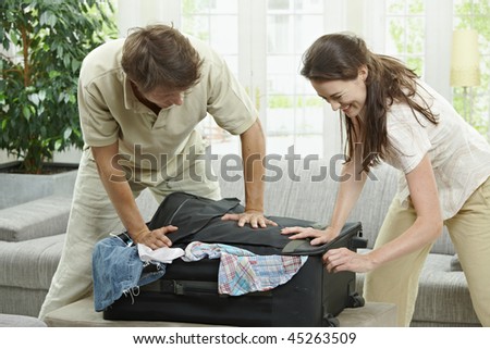 Couple packing for holiday, trying to close suitcase full with clothes.