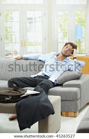 Tired businessman resting on couch at home after long day of work.