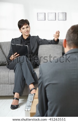 Business meeting at office. Female consultant sitting on sofa talking to partner, smiling.