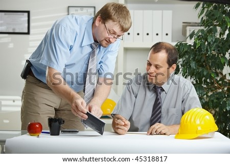 Engineers working at office - planning and talking over blueprint on desk.
