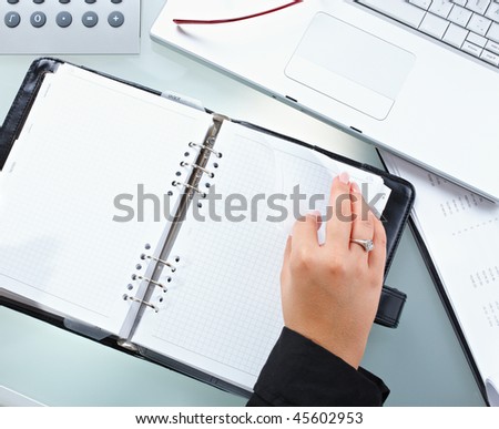 Female hand turning page of a notebook, holding pen.