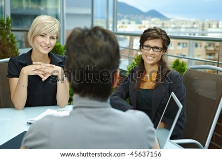 Happy young businesswomen sitting around table outdoor on office terrace and talking, smiling. Over the shoulder view.