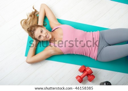 Young woman lying on fitness mat at home, smiling. Overhead shot.