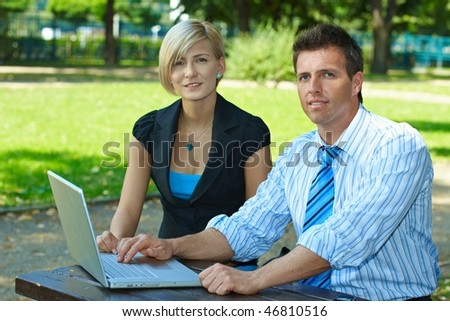 Young businesspeople using laptop computer outdoor in city park, smiling.