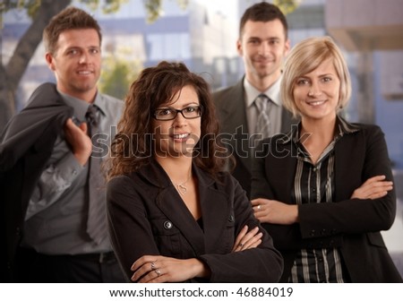 Portrait of young businesswoman standing outdoor with colleagues, smiling.
