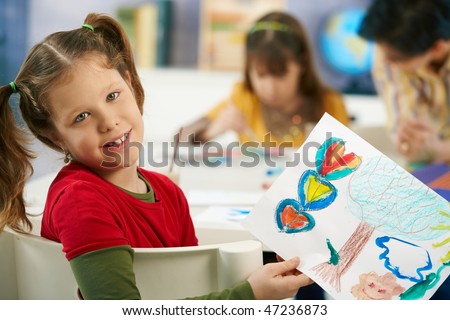Portrait of elementary age schoolgirl showing colorful paining to camera in art class in primary school classroom.