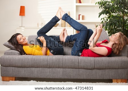 stock photo Smiling teens lying on couch with feet put together playing
