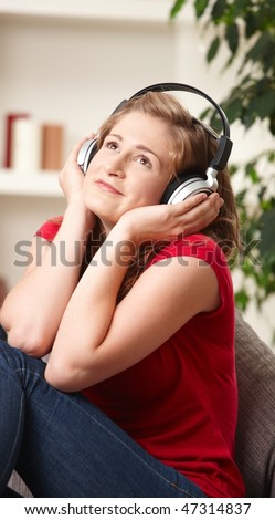 Happy teen girl listening to music on headphones sitting on couch at home smiling.