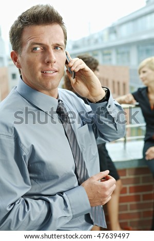 Business people talking on terrace outdoor of office building. Businessman in front using mobile phone.