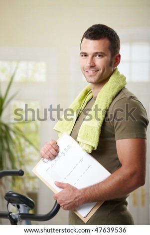 Man wearing sportswear standing in living room at home, holding training plan.