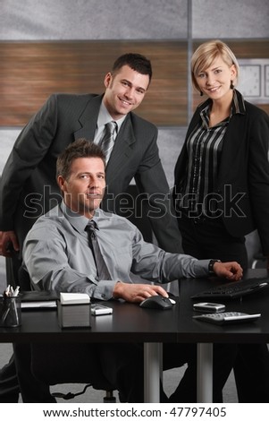 Portrait of happy businessman and team at office desk, looking at camera, smiling.