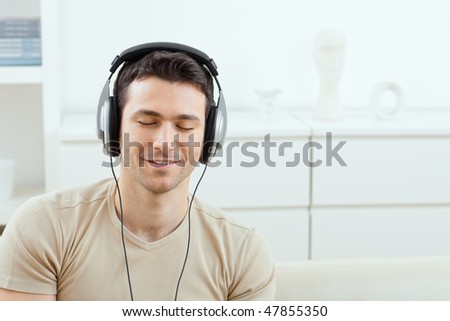 Casual man listening music with headphones at home, relaxing with closed eyes, smiling.