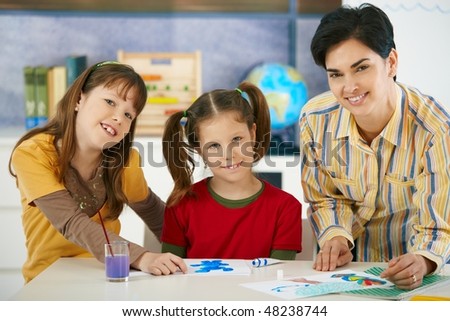Portrait of elementary age children and teacher in art class in primary school classroom. Looking at camera, smiling.