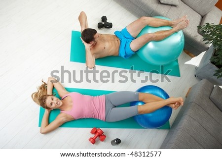 Young couple doing abdominal crunch using fit ball at home, overhead shot.