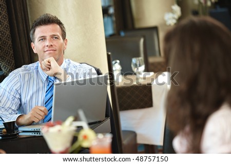 Businessman sitting at table in cafe using laptop computer, thinking.