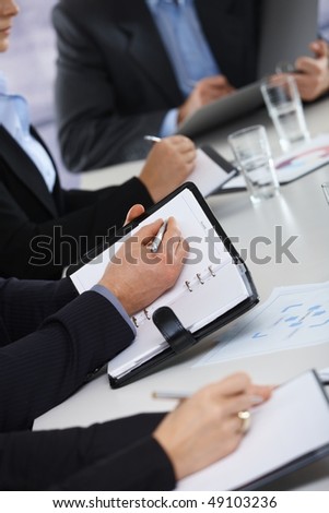 Closeup of hands on business meeting at office writing notes to personal organizer,