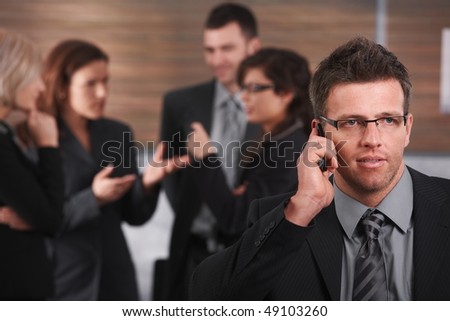 Portrait of businessman talking on mobile phone, business people discussing in background.