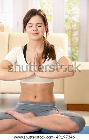 Girl doing yoga meditation sitting on living room floor with closed eyes, smiling.