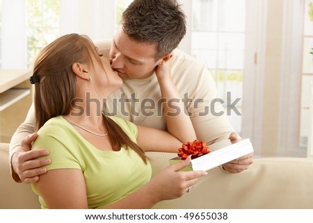 Kissing couple sitting on sofa, man handing present over to woman.