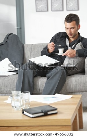 People at office. Tired businessman sitting on sofa looking at documents drinking coffee.