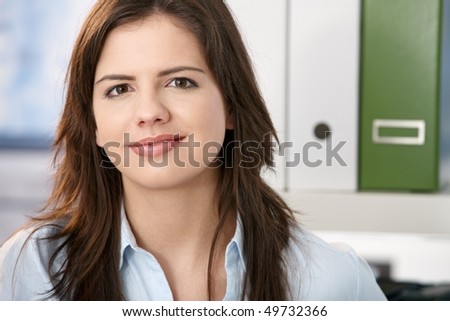 Pretty professional girl smiling at camera, face in closeup, office background.