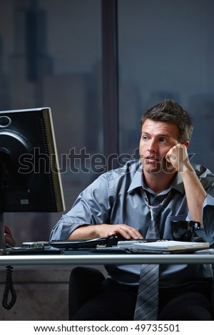 Tired professional businessman looking at computer screen troubled, thinking at office desk working overtime.