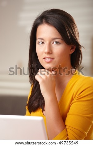 Teenage girl looking at camera thinking sitting at table with hands folded under chin.