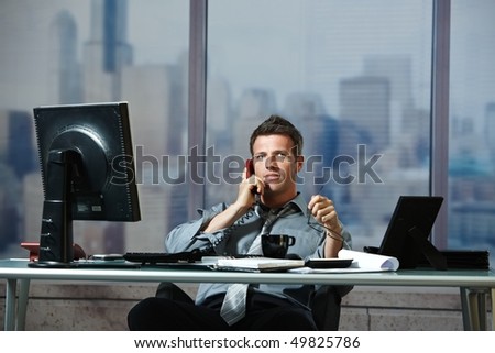 Mid-adult successful smiling businessman calling on landline listening to conversation sitting at office desk.