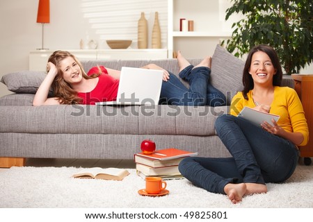 Happy schoolgirls studying together in living room with books and computer, laughing.