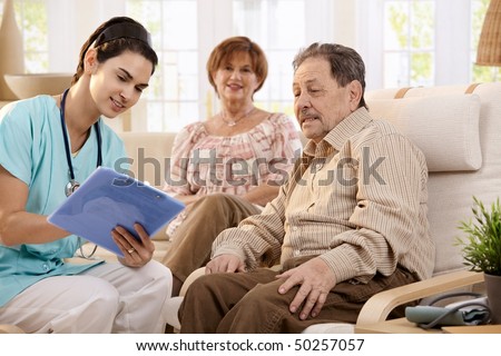 Nurse talking with elderly people and making notes during examination at home, smiling.