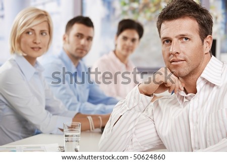Satisfied businessman sitting at table in meeting room at office, looking at camera.