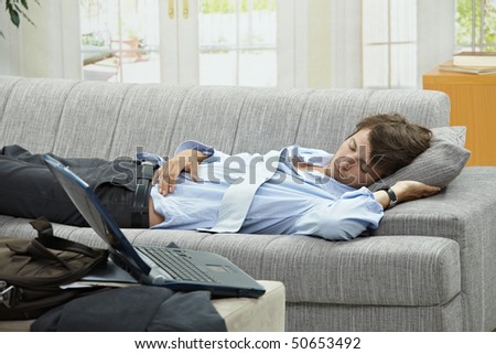 Tired businessman resting on couch at home after long day of work.