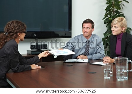 Business people sitting around meeting table in board room, talking.