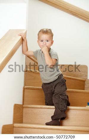 Worried little boy standing on stairs, leaning on hand rail.