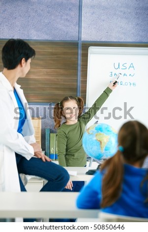 Elementary age schoolgirl at whiteboard answering to teacher in geography lesson.