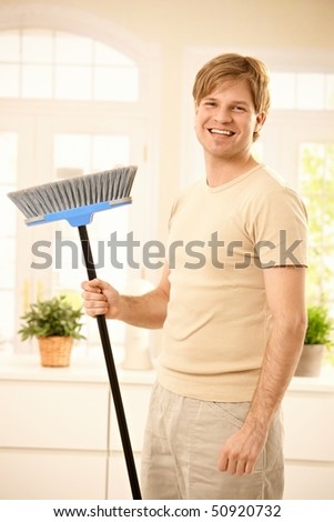Happy guy laughing at camera, holding broomstick standing in living room.