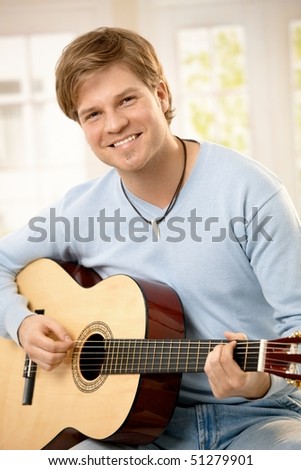 Portrait of handsome guy playing guitar, looking at camera, smiling.