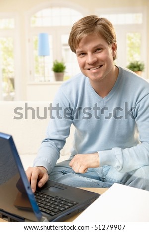 Portrait of happy young man using computer, browsing on internet, smiling.